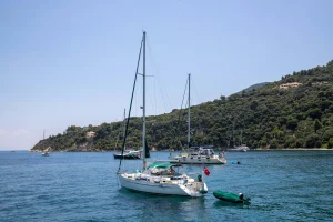 A monohull sailboat anchored in a calm bay along a green island coastline in Greece, ideal for traditional sailing in the Ionian Sea.