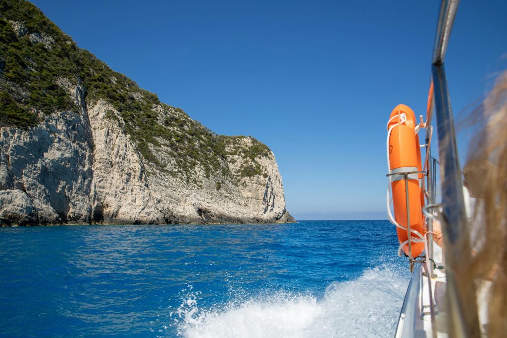 Boat cruising past rocky cliffs with clear blue sea and sky in the Ionian Islands
