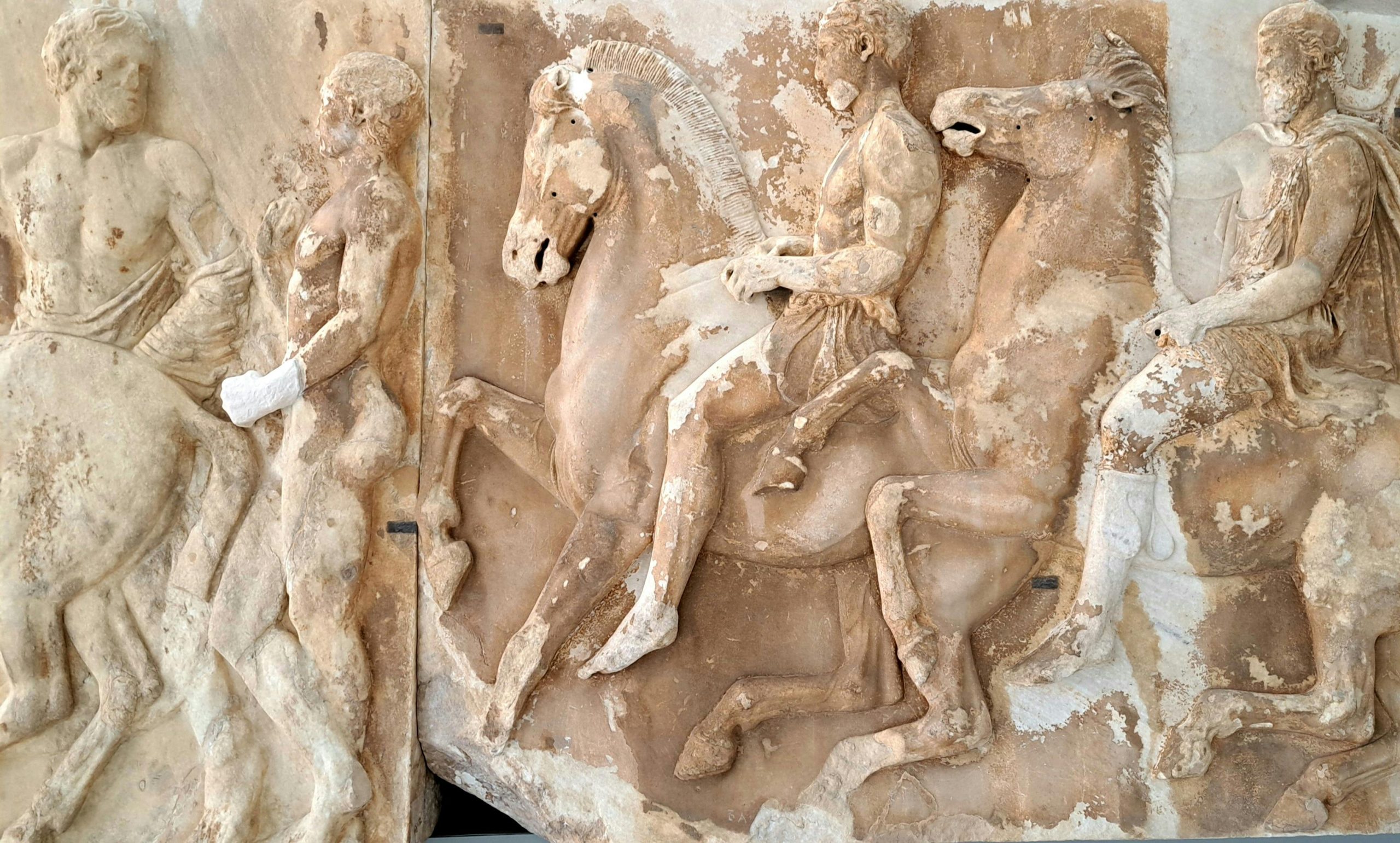 Ancient Greek marble relief depicting horsemen and figures, showing classical art and mythology
