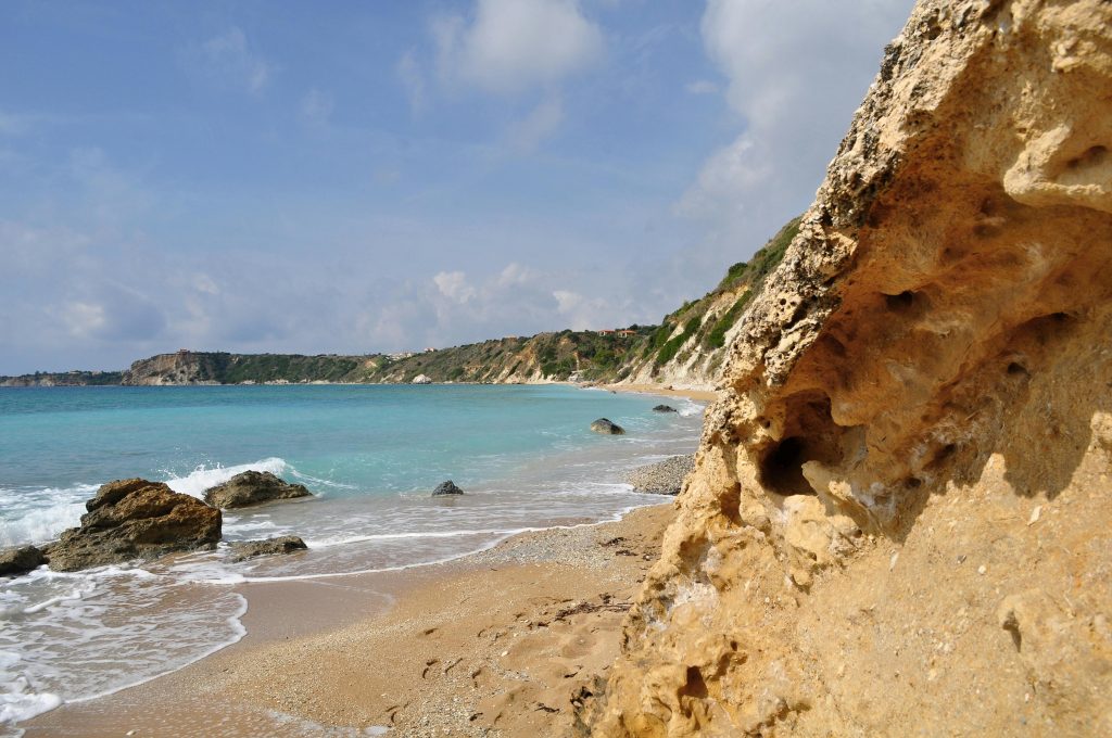 Golden sandy beach with rocky formations and turquoise waves on Kefalonia island, Greece.