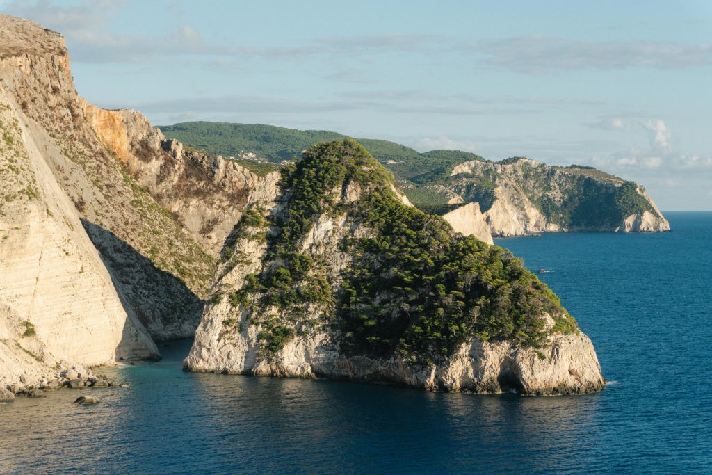 Rocky coastal cliffs covered with greenery rising above turquoise waters in the Ionians, Greece.
